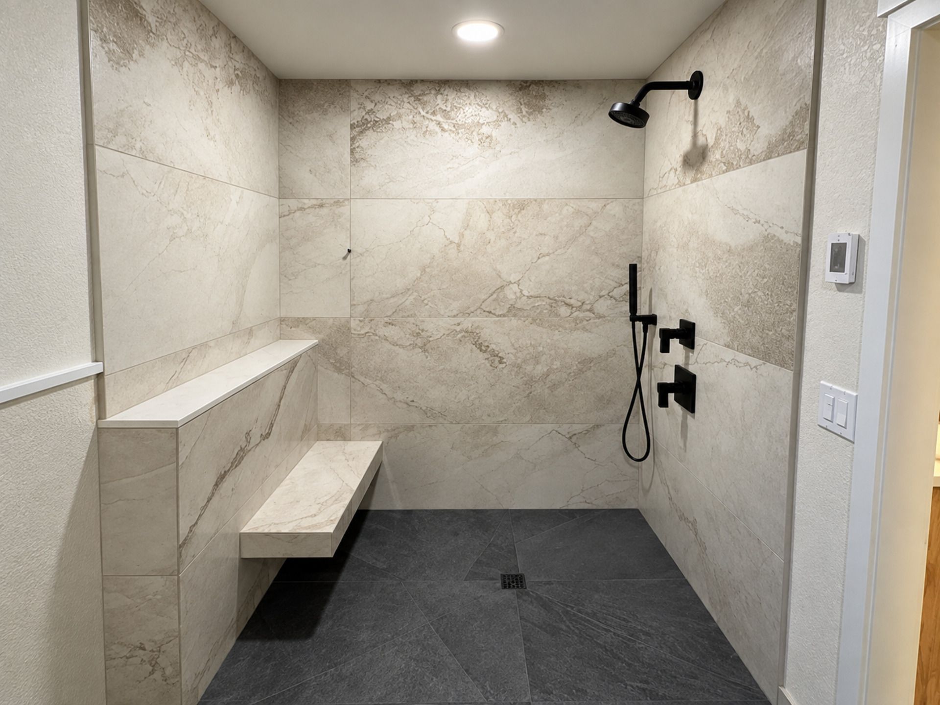Alderwood Builders walk-in shower remodel in Ferndale, WA with marble-look tile, floating bench, and black fixtures.
