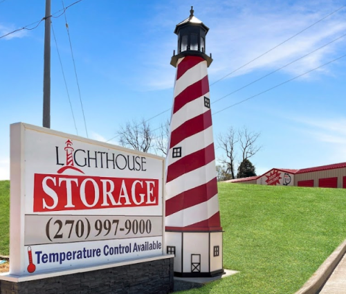 Lighthouse Storage sign beside a red-and-white striped lighthouse tower on a grassy hillside