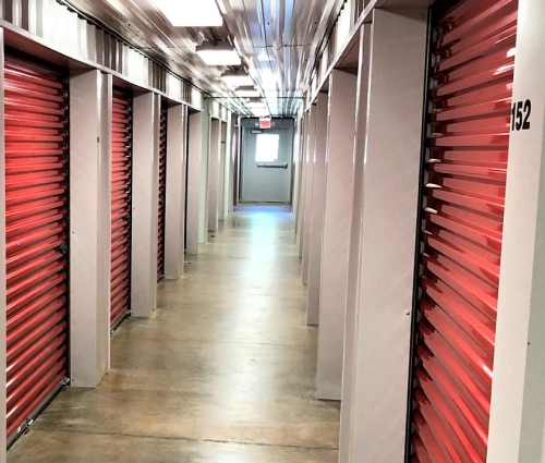 Storage facility hallway with red roll-up unit doors and a concrete floor