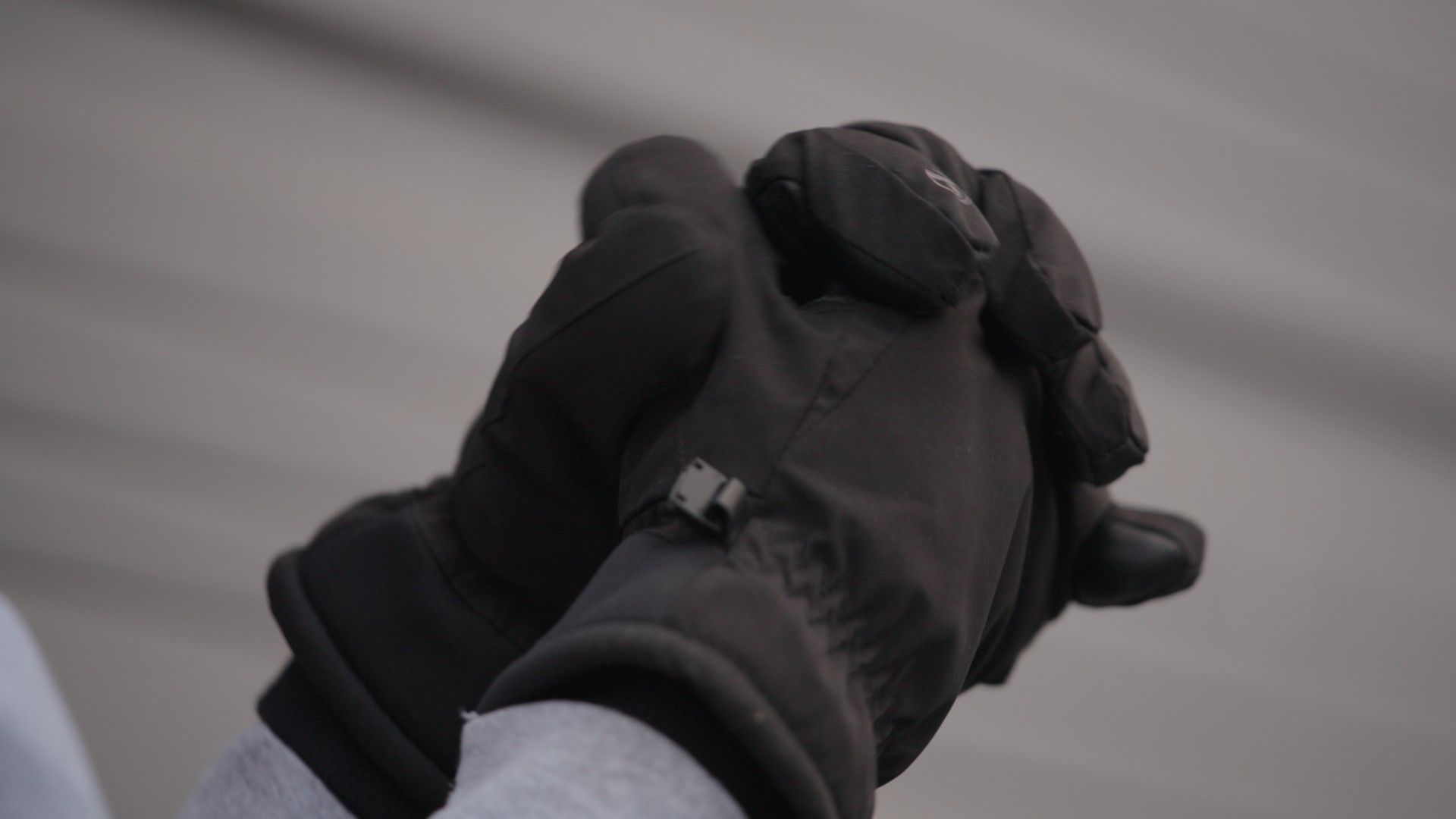 A person wearing black winter gloves with their hands clasped together.