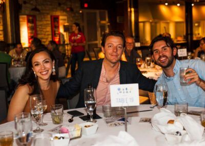 Three people smile at a table at an event, with a sign reading