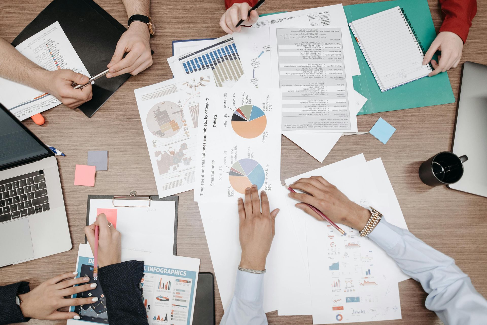Overhead view of a group collaborating around a table filled with business documents, charts, and a laptop.