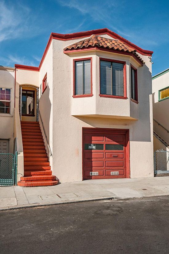 Two-story stucco house with red trim, a bay window, and a garage door on a sunny day.