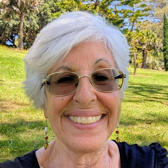Smiling person with white hair and glasses outdoors in a sunny park