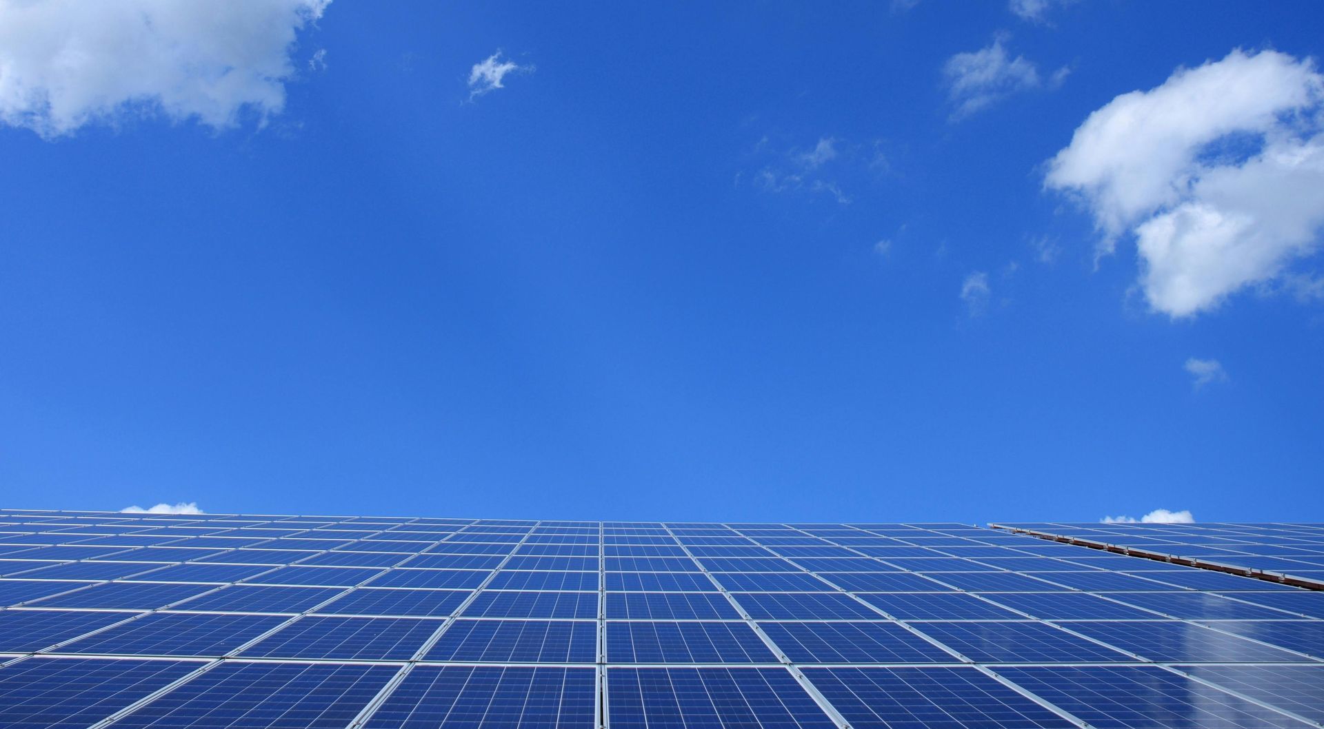 Uma fileira de painéis solares contra um céu azul com nuvens.