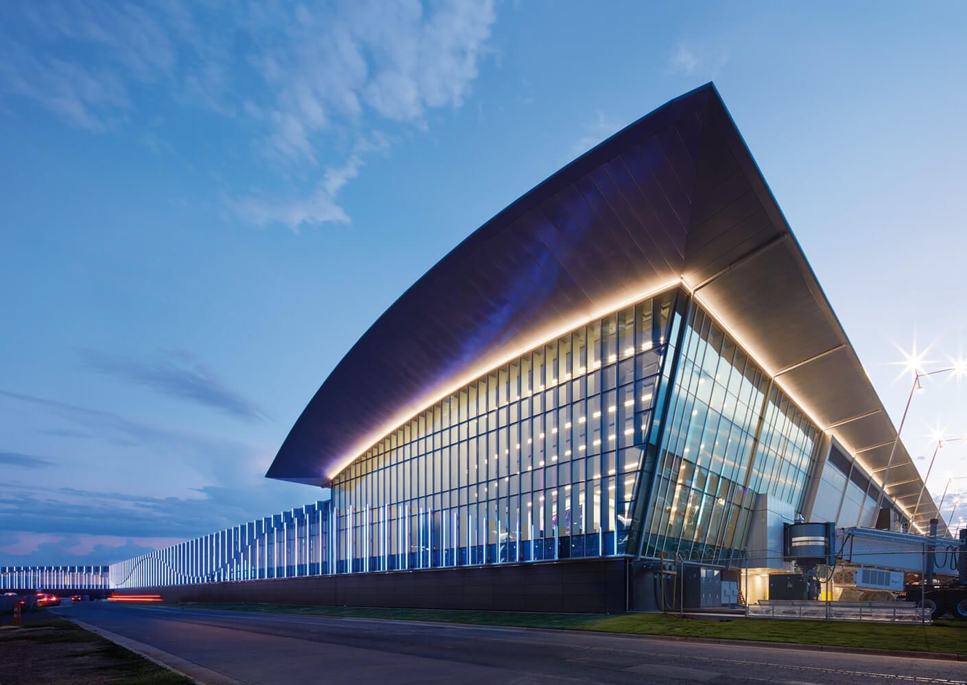 Modern building with large glass windows and curved roof, lit up at dusk.