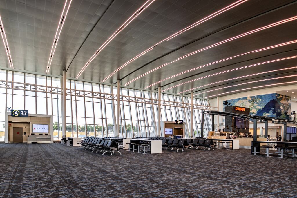 Modern airport terminal interior with rows of seating, large windows, and overhead lighting.
