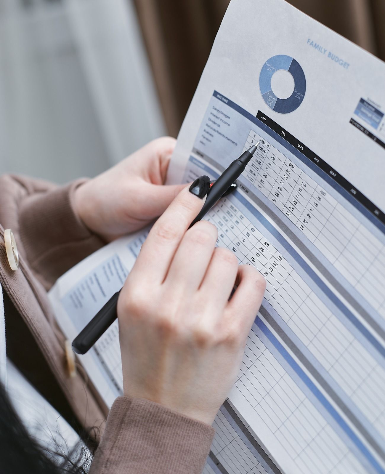 Person writing on a financial report with a pen, reviewing charts and spreadsheet data on paper.