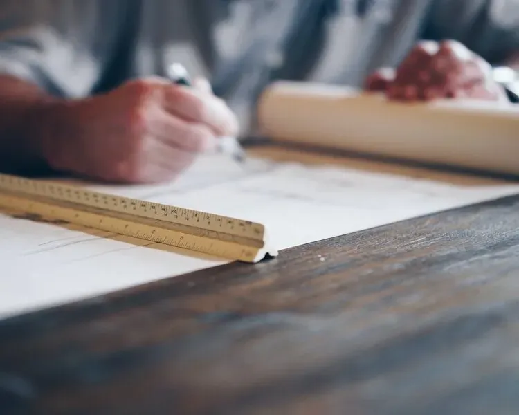 A person is writing on a piece of paper next to a ruler.