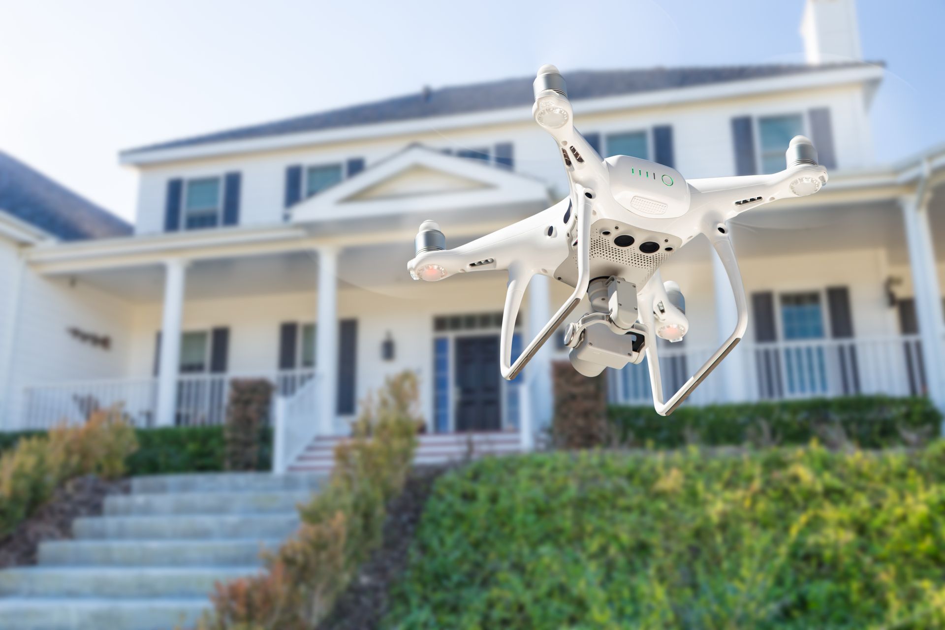 A drone is flying in front of a large white house.