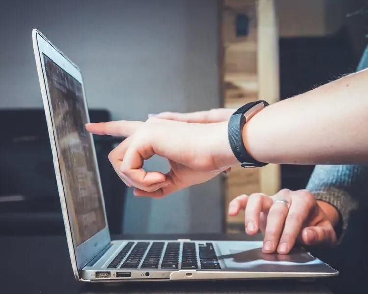 A person is using a laptop computer and pointing at the screen.