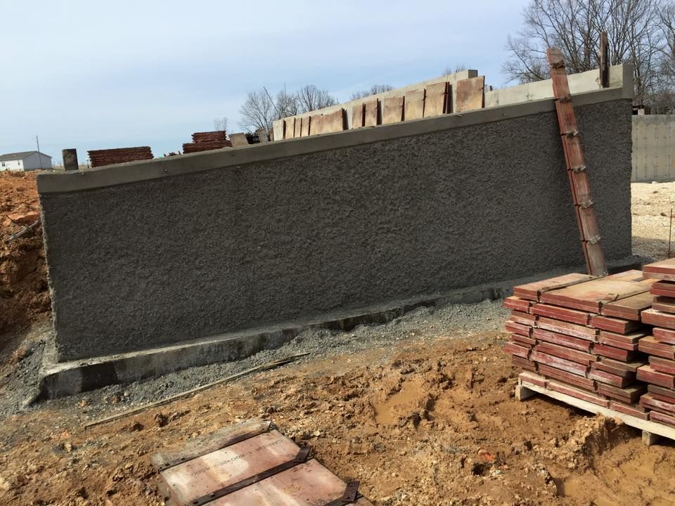 Curved stone wall under construction, with stacked bricks and dirt foreground outdoors.