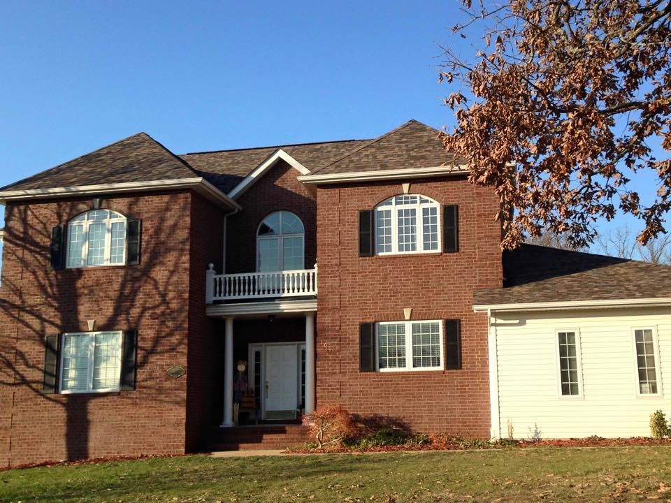 Two-story brick house with white side addition, arched windows, and a front porch under a clear blue sky