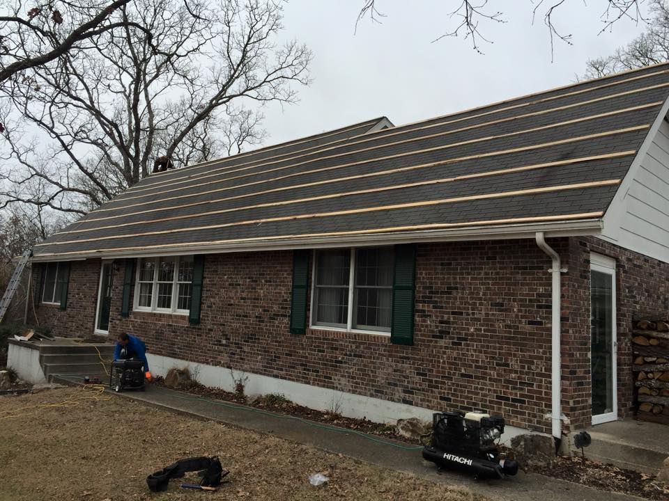 Brick house with new dark roof being installed, with ladders and tools in the yard