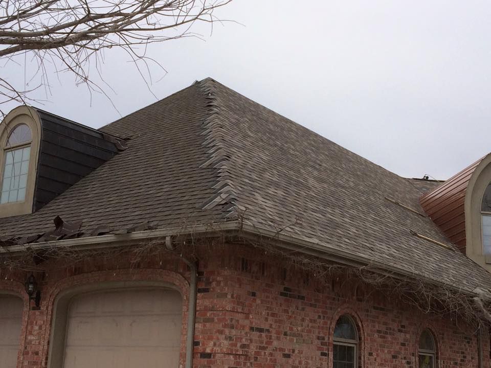 Brick house with a steep shingled roof and arched window under bare tree branches