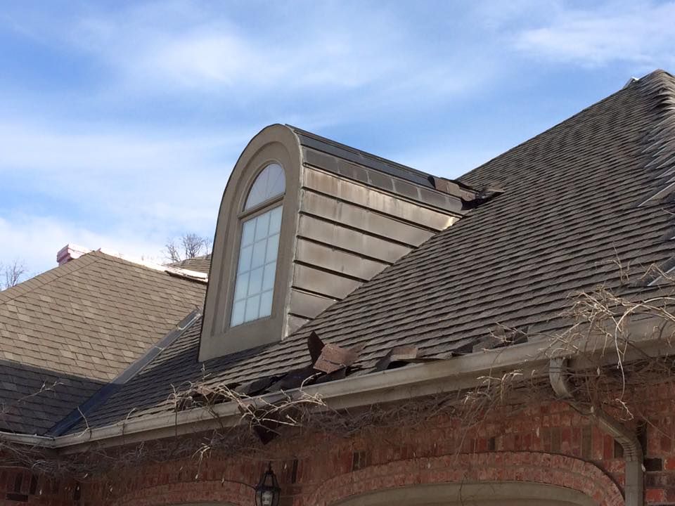 Dormer window on a shingled brick house roof under a blue sky