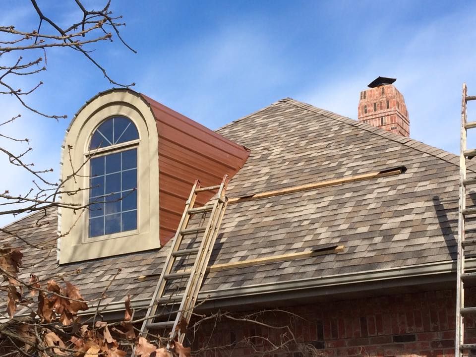Roof with two ladders, a dormer window, and a brick chimney under a blue sky.