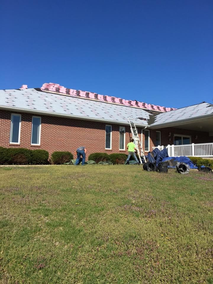 Workers repairing a brick house roof with exposed insulation on a sunny day