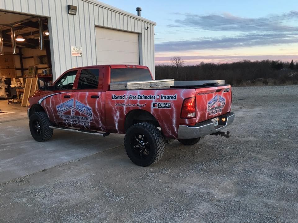 Red pickup truck with custom graphics parked outside a shop at dusk
