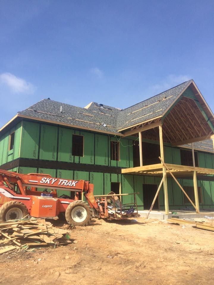 Partially built house with green sheathing and a red Sky Trak forklift on a dirt lot