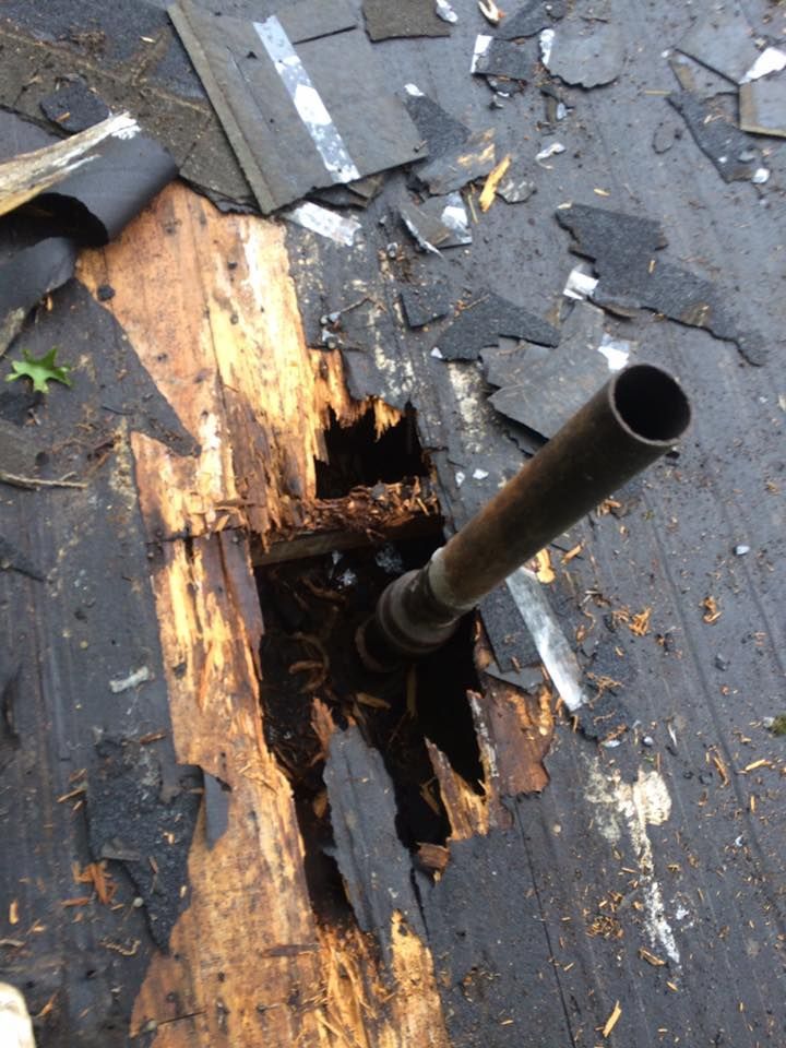 Damaged roof with a large hole around a black vent pipe and torn shingles