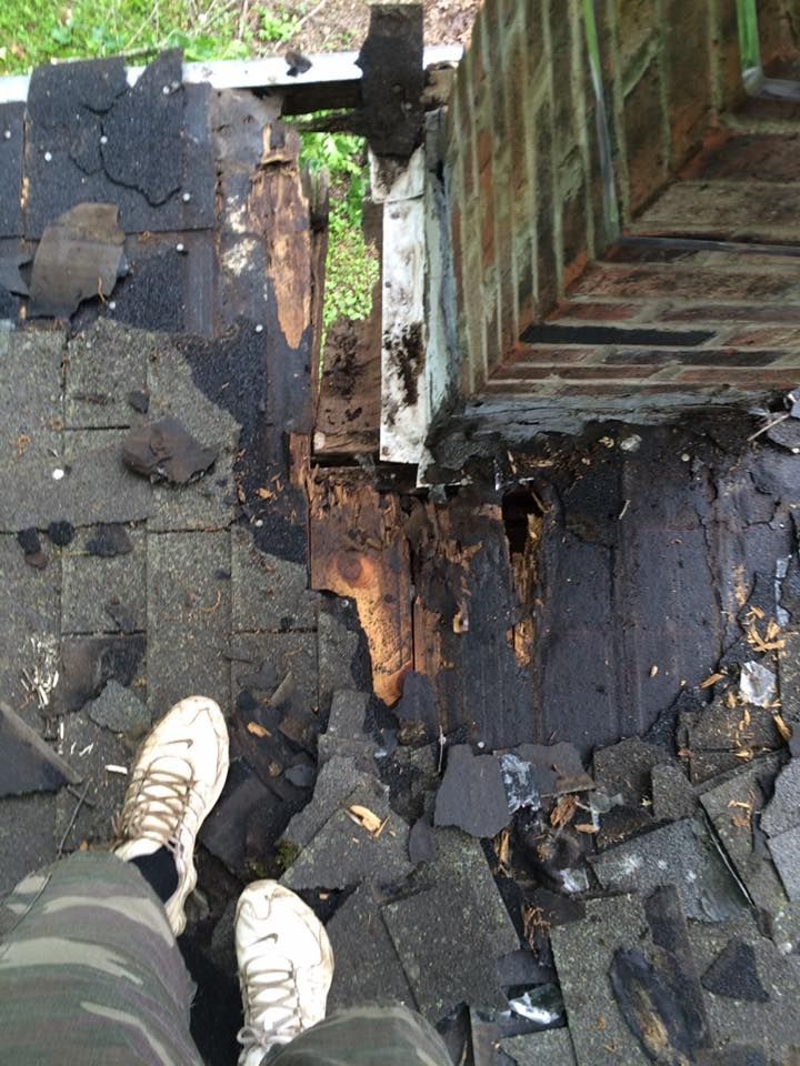 Looking down at a damaged rooftop with broken shingles and a person’s shoes at the edge of a gap