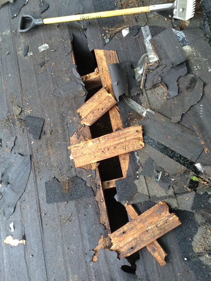 Damaged roof shingles with a long hole exposing wooden supports and a hammer lying nearby