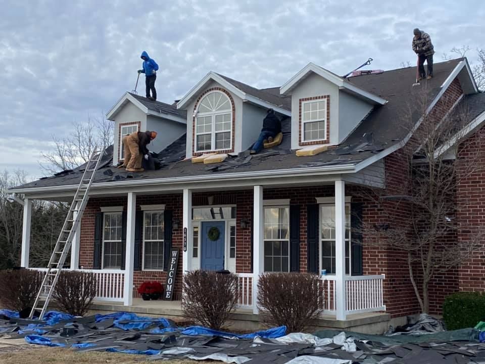 Workers repairing a house roof after storm damage, with ladders and blue tarps on the ground