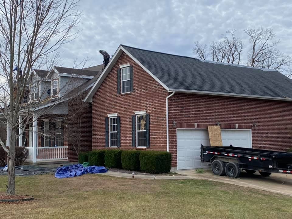 Brick house with white garage, black trailer in driveway, and blue tarp on the lawn.