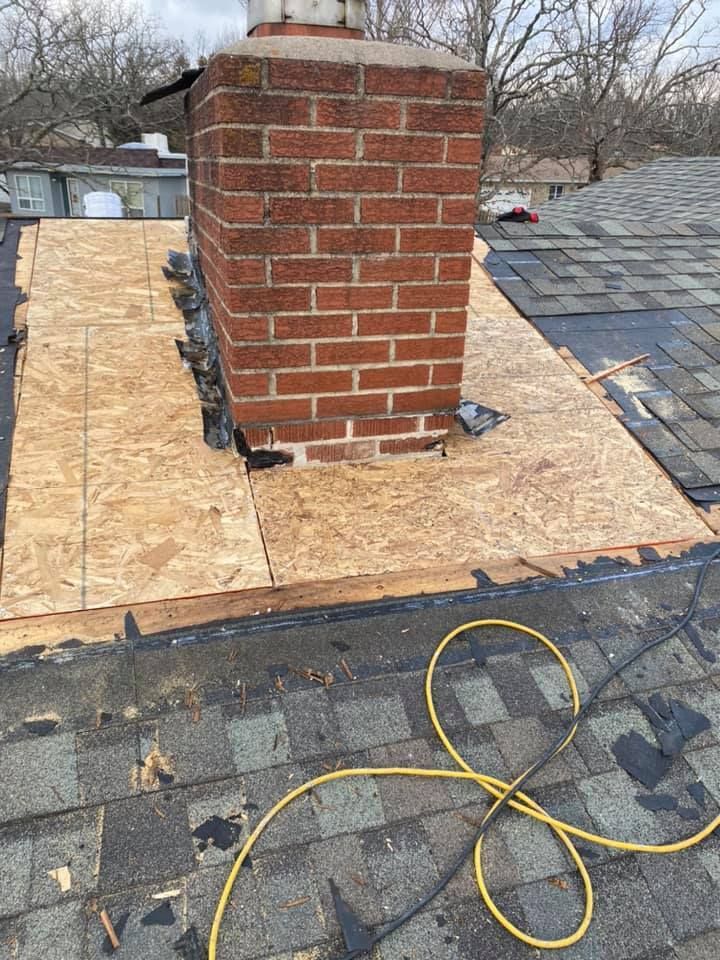 Brick chimney on a roof with plywood and shingles, and a yellow extension cord in the foreground