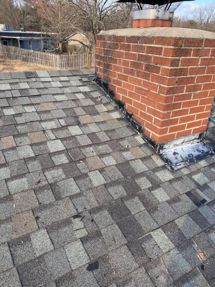 Rooftop with gray shingles and a red brick chimney beside a fenced yard.