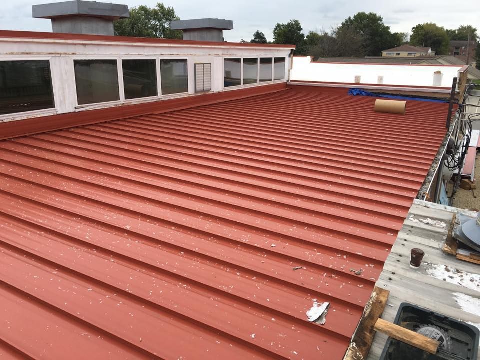 Red corrugated metal roof on a building with skylights and a rooftop vent under an overcast sky