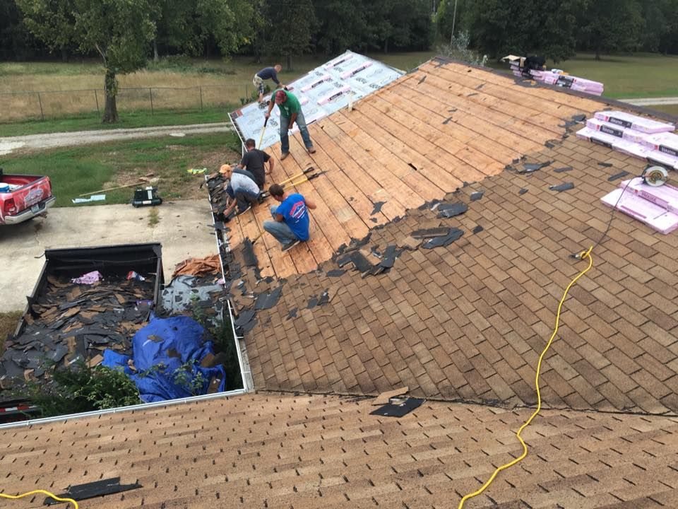 Workers repairing a shingled roof, with stacks of materials and a yellow extension cord on the roof.