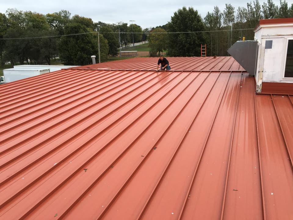 Red metal roof with a small roof vent and trees in the background
