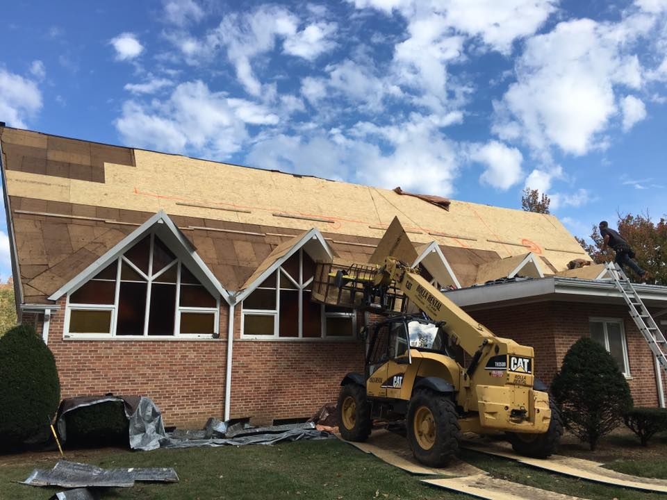 Construction loader lifting roof on damaged brick building under blue sky