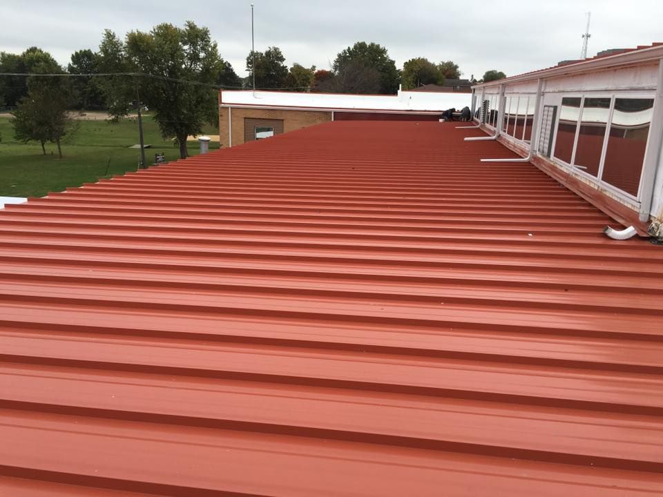 Red metal roof on a building with trees and cloudy sky in the background