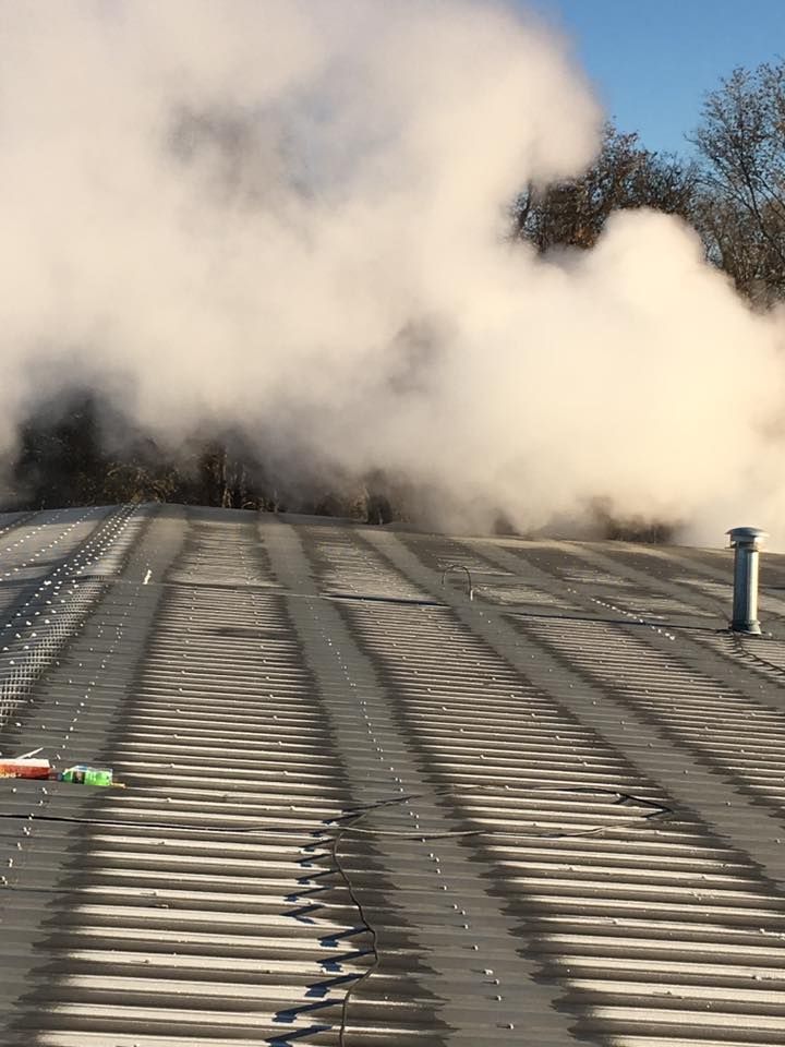 Smoke rising over a road or railway crossing, with tracks and a small post in the foreground