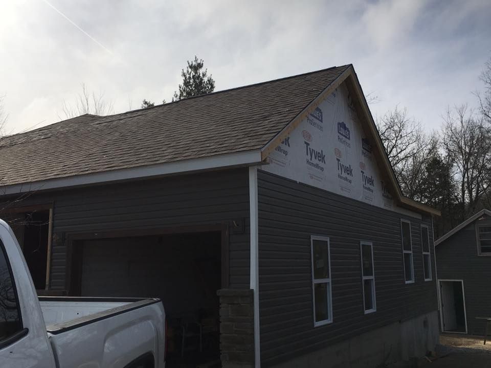 Dark gray house with unfinished gable siding and a pickup truck parked beside it
