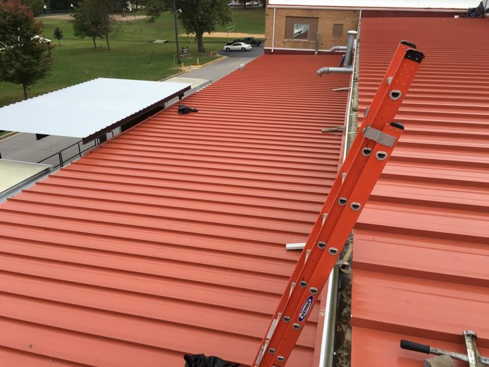 Orange metal roof with ladders leading to a brick building in a park-like setting