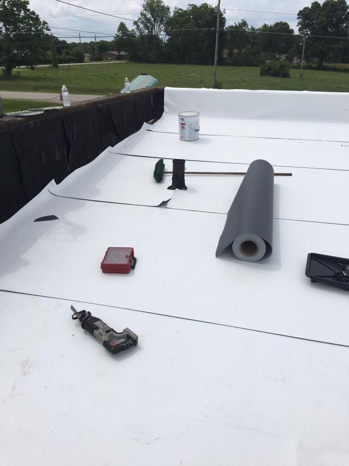 Flat white commercial roof with HVAC materials and tools, including a rolled membrane and bucket.
