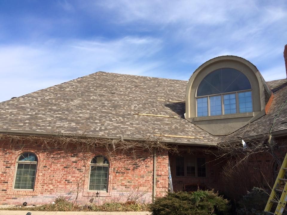 Brick house with gray roof and large arched dormer window under a blue sky