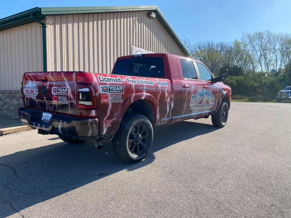 Red pickup truck with precision roofing decals parked beside a metal building on a sunny day
