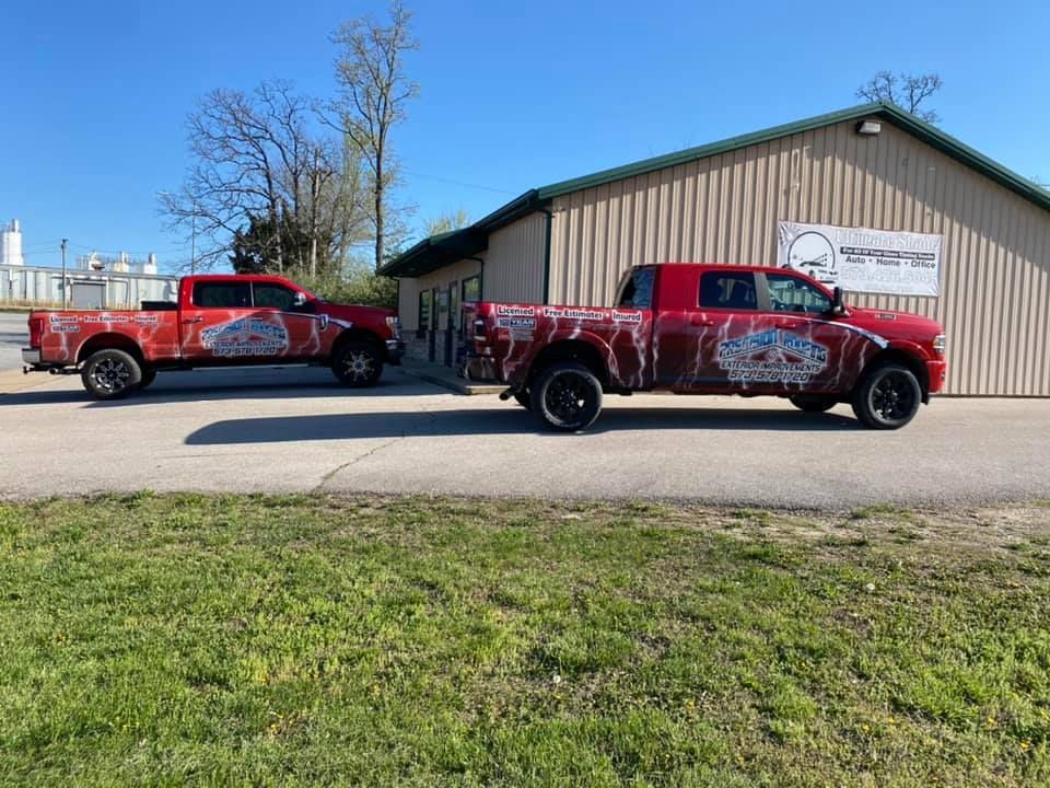 Two red pickup trucks parked beside a metal building on a sunny day