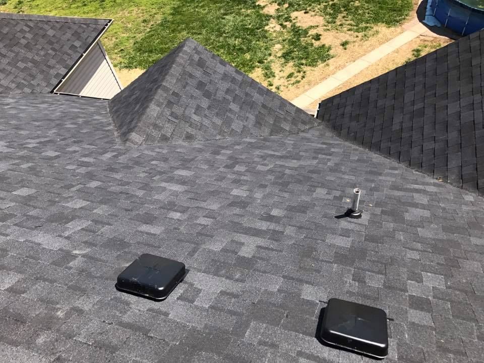 Gray shingled roof with two black vents and a small pipe under daylight