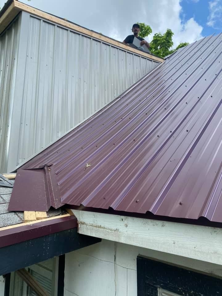 Metal roof being installed on a white building, with a worker visible at the ridge edge.