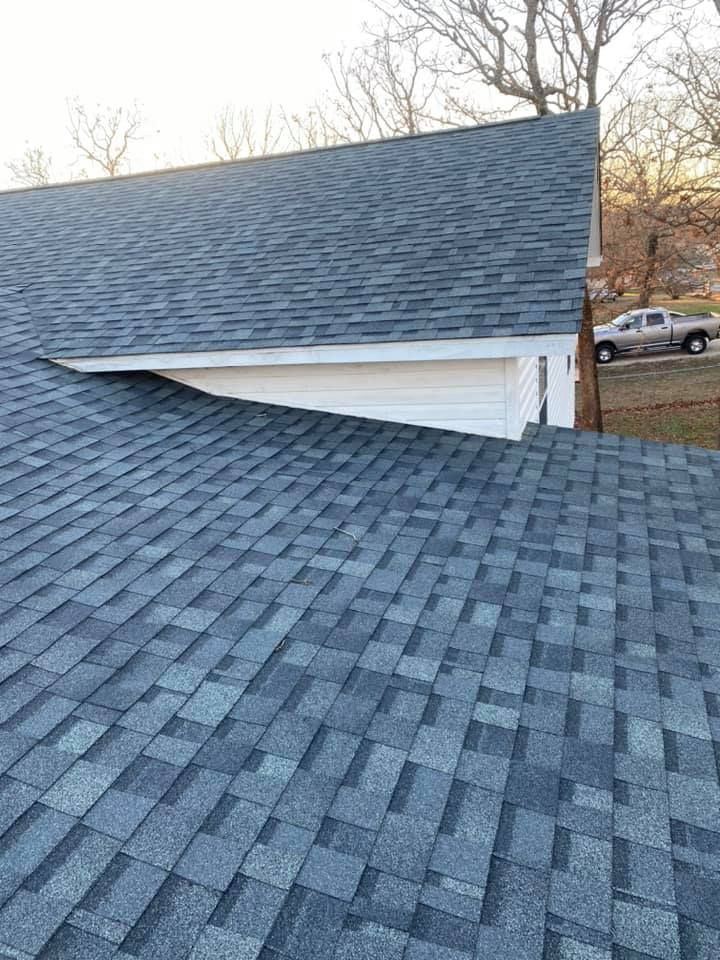 Close-up of blue-gray shingle roofs meeting at a white gable on a house at sunset.
