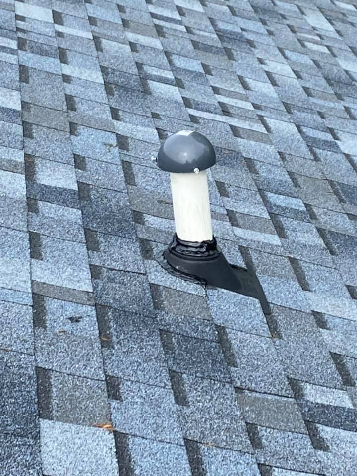 Rooftop vent pipe with a dark cap on gray shingles, casting a shadow.