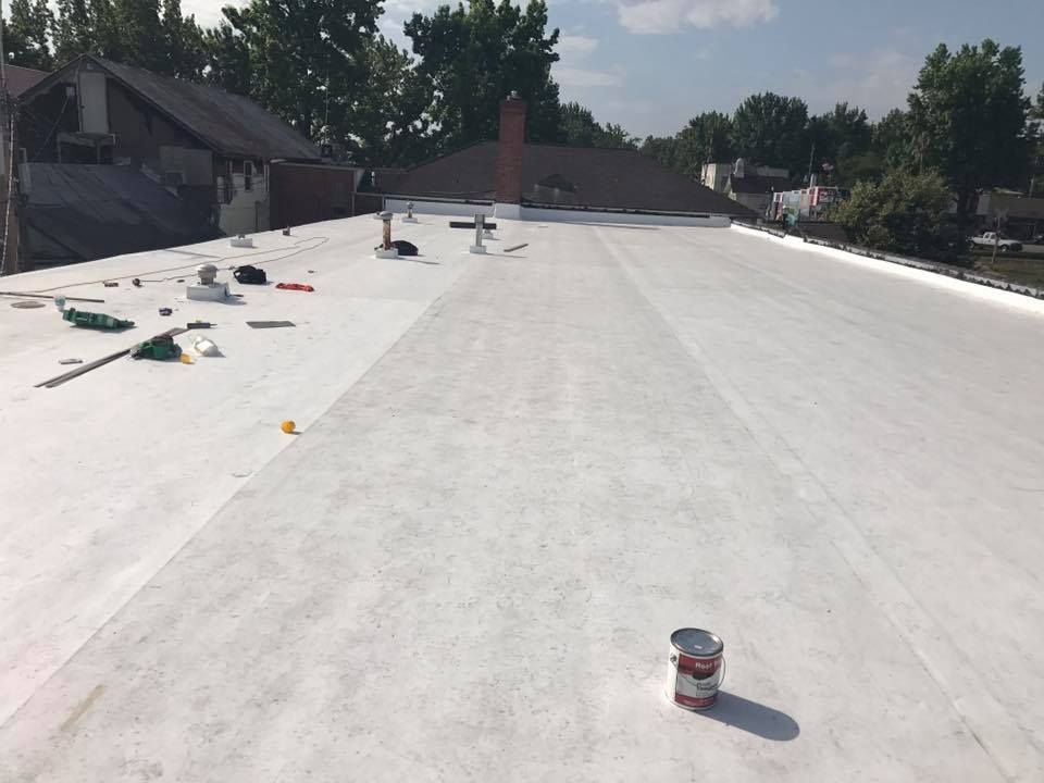 Workers on a white flat roof, with tools and supplies scattered across the surface.