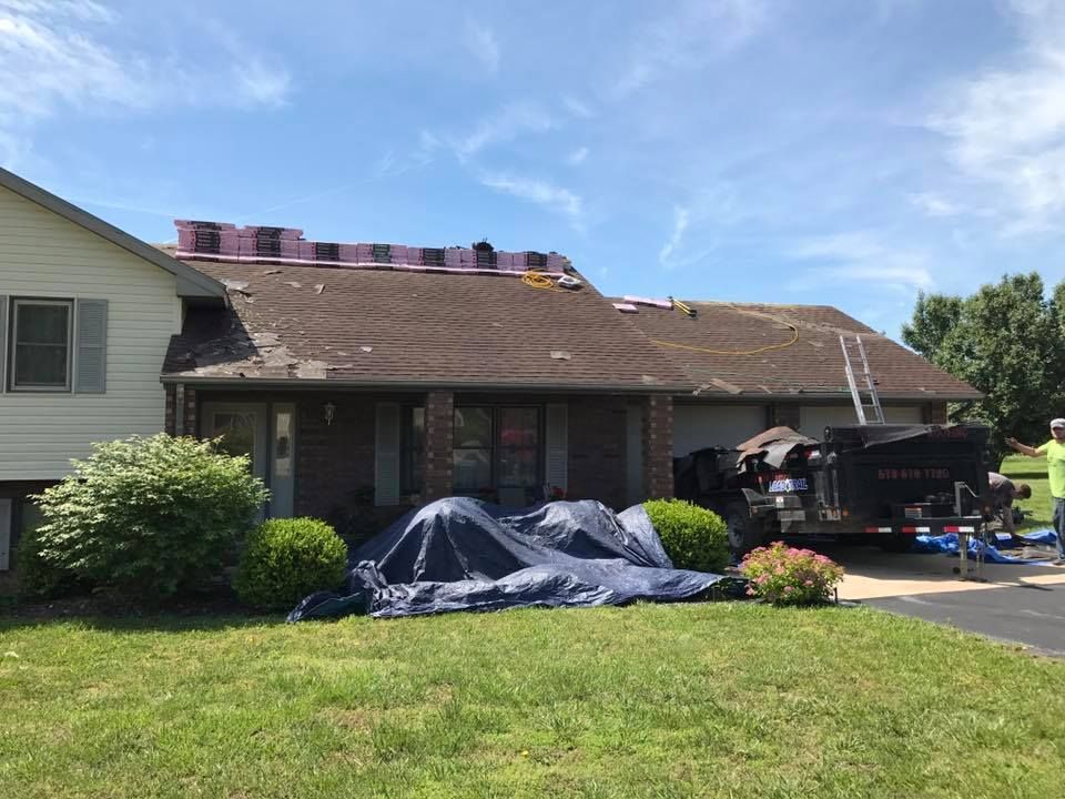 House roof under repair with tarps, debris, and a worker’s truck in the driveway