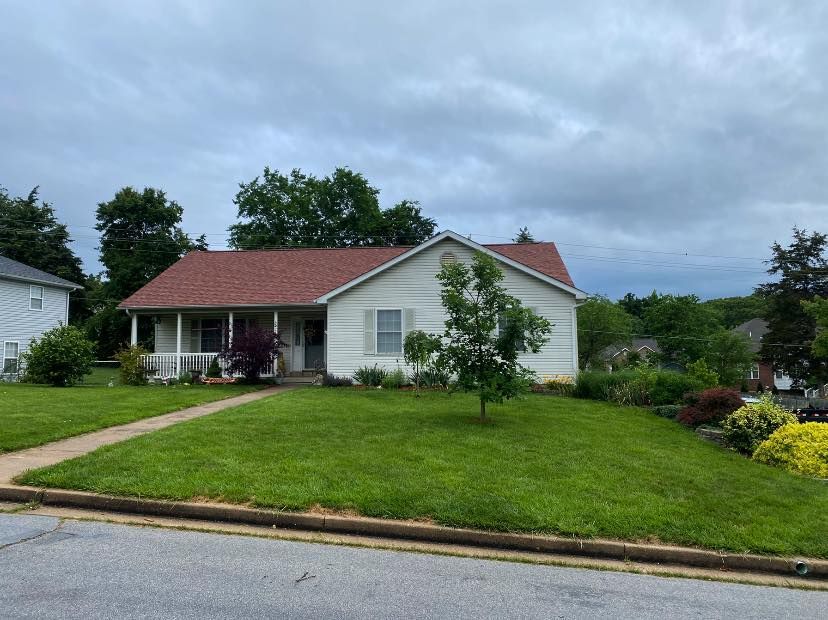 Single-story house with red roof, white siding, and green lawn under a cloudy sky